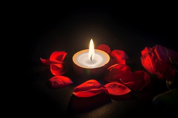 Tea candle, red rose and rose petals on black