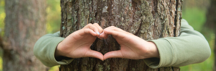 Child's hands making a heart shape on a tree trunk