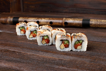 Fresh sushi roles on a wooden plate with hands of the chef in the background