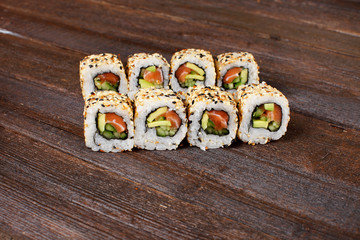 Fresh sushi roles on a wooden plate with hands of the chef in the background