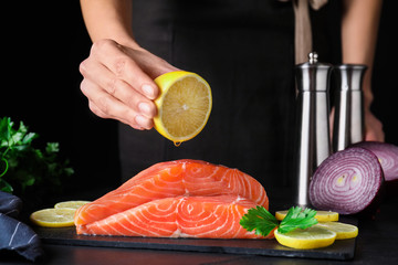 Woman squeezing lemon onto fresh raw salmon at table, closeup. Fish delicacy