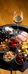 Cheese and fruits plate with glass of white wine on round tray, colorful and delicious charcuterie with snacks and wineglass for romantic evening, wine tasting, selective focus.