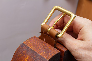 sewing handmade brown leather belt with hands needle thread