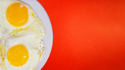 Fried eggs from two eggs close-up on a light plate, on a red background. The concept of fun food.