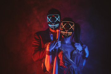 Portrait of elegant couple in scary masks with baseball bat in hands.