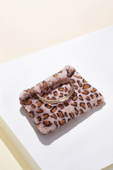 Object shot of a pale pink leopard print faux fur bag with metallic semicircular bag handles, lying on a white surface. The bag is casting a shadow.