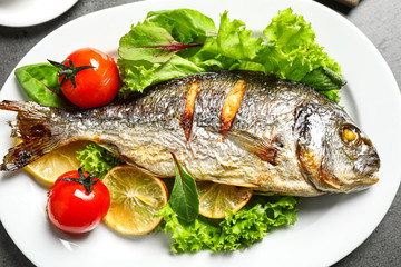 Delicious roasted fish with lemon and vegetables on plate, closeup view