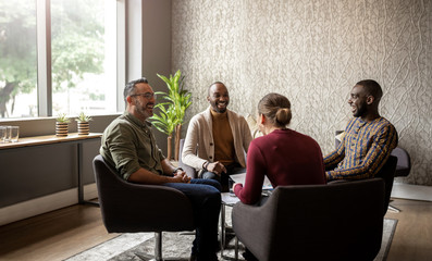 Casual seated diverse business meeting in modern open workspace with large windows and sunlight...