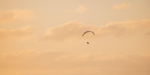 Paraglider floating through golden blue sunset or sunrise sky over Camps Bay, Cape Town.