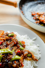 Portion of stir fry vegetables and rice on a white plate with frying pan in background