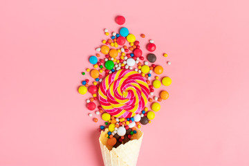 mix colorful chocolate sweets spilled out of ice cream waffle cone on pink background Flat lay Top...