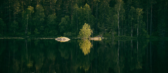 Panorama of a lake with a small island and with forest in the background and reflections in the water from the forest
