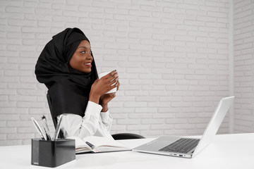 Side view of smiling woman in black hijab drinking coffee