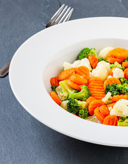 Gemüseteller mit Kaisergemüse: Möhren, Blumenkohl und Brokkoli auf dunkler Schiefertafel