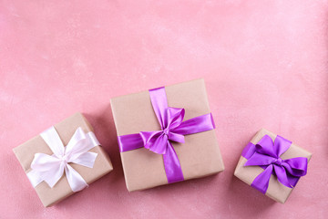 Simple composition with multiple presents wrapped in hand made blank craft paper gift wrap, pastel satin bow. Simple giftbox, wrapping, giftwrap, silk ribbon. Pink background, close up, copy space.