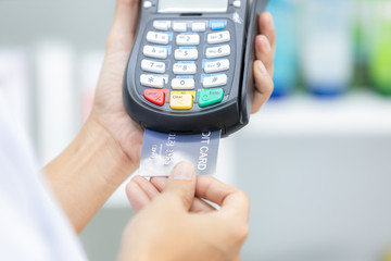 Paying with a credit card, Making purchases many medicines, Paying with a credit on many medicines shelf in pharmacy background.