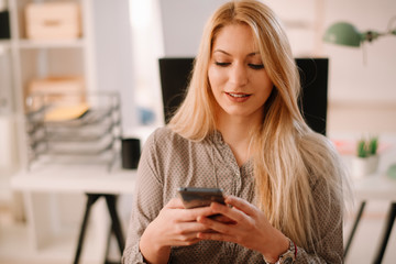 Young businesswoman in office. Beautiful woman using phone at her workplace.