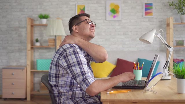 Young woman sitting at a laptop feels a pain in the neck and back due to stooping