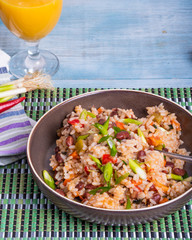 Traditional Mexican dish - rice with beans and vegetables with chili peppers and green onions in a bowl and a glass of juice on a bamboo napkin, tasty and healthy vegetarian dish