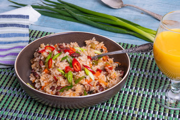 Traditional Mexican dish - rice with beans and vegetables with chili peppers and green onions in a bowl and a glass of juice on a bamboo napkin, tasty and healthy vegetarian dish