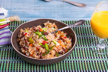 Traditional Mexican dish - rice with beans and vegetables with chili peppers and green onions in a bowl and a glass of juice on a bamboo napkin, tasty and healthy vegetarian dish