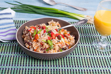 Traditional Mexican dish - rice with beans and vegetables with chili peppers and green onions in a bowl and a glass of juice on a bamboo napkin, healthy vegetarian dish