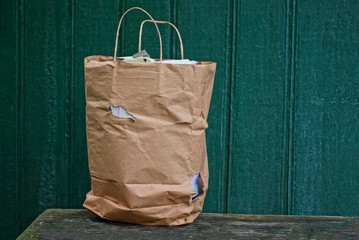 a full old brown paper bag with a hole is standing on a table against a green wall