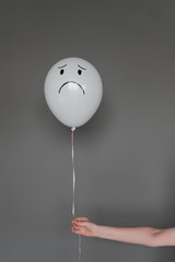 Balloon with sad emotion in a human hand on a gray background.