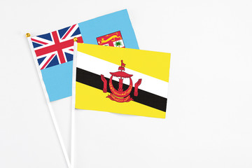 Brunei and Fiji stick flags on white background. High quality fabric, miniature national flag. Peaceful global concept.White floor for copy space.