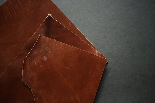 Selected pieces of beautifully tanned or colored leather on dark grey background. Leather work or craftmanship.