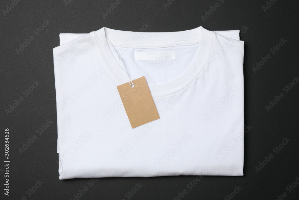 Wall mural Folded blank white t-shirt with tag on black background, space for text