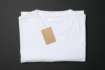 Folded blank white t-shirt with tag on black background, space for text