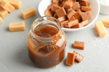 Glass jar with salted caramel and candies on grey background, close up