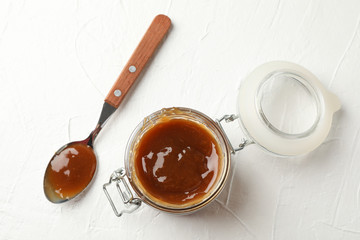 Glass jar with salted caramel and spoon on white background, top view