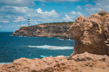 Fototapeta na wymiar Moscarter lighthouse on the Ibiza island in the Mediterranean sea on top of a cliff shot from coast, wide landscape with rocky coast in foreground