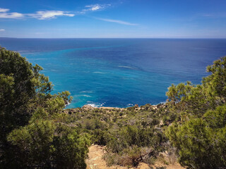 Fototapeta na wymiar View of Ibiza coastline from top of a rocky hill at Sa Pedrera de Cala D'Hort. Trees and green Mediterranean Conifers in the foreground view from high point top calm sea turquoise water