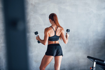 Young fitness woman with slim type of body and in black sportive clothes is in the gym