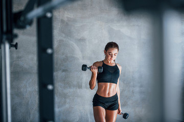 Young fitness woman is in the gym with dumbbells in hands