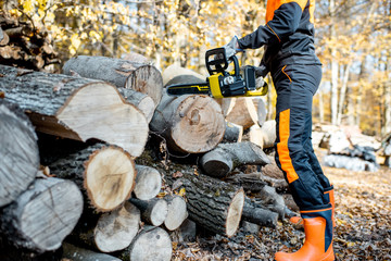 Fototapeta premium Professional lumberjack in protective workwear working with a chainsaw in the forest, sawing wooden logs, close-up view with no face