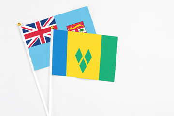 Saint Vincent And The Grenadines and Fiji stick flags on white background. High quality fabric, miniature national flag. Peaceful global concept.White floor for copy space.