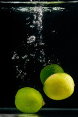 Fototapeta na wymiar Green limes in water on a black background.