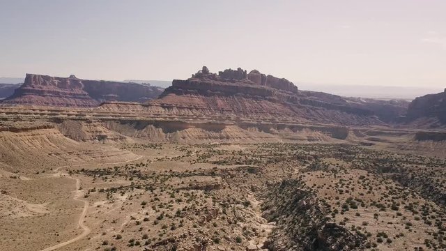 Incredible beautiful drone footage flying away from mesa rock over desert valley, bushes and landscape in Black Dragon Canyon in Green River, Utah, United States