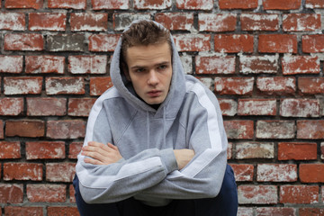 Fototapeta na wymiar portrait of a dangerous teenager in a hood against a brick wall