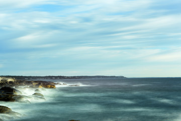 The coast of the Atlantic Ocean. Waves breaking on stones, the running of clouds and water underlined by a long exposure. Minimalistic seascape. USA. Maine