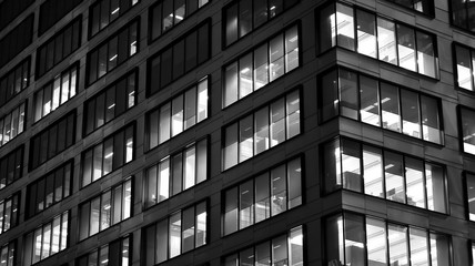 Fototapeta na wymiar Pattern of office buildings windows illuminated at night. Lighting with Glass architecture facade design with reflection in urban city. Black and white.