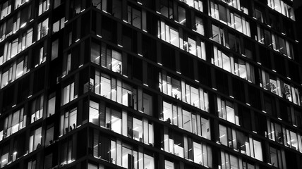 Obraz premium Pattern of office buildings windows illuminated at night. Lighting with Glass architecture facade design with reflection in urban city. Black and white.