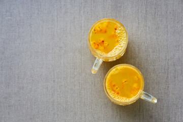 Sea buckthorn tea in glass mugs on brown textile background