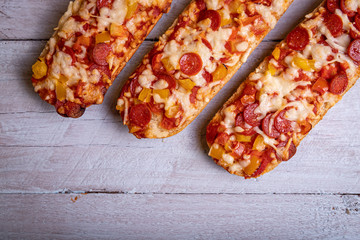 Pizza baguettes with salami and white wooden background