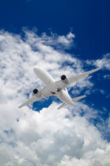 Fototapeta na wymiar white passenger plane flies against backdrop of beautiful white clouds on blue sky