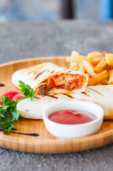 Burrito rolls and fries with ketchup on a wooden plate.